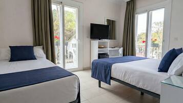 Habitación de hotel con dos camas, televisión y balcón con vistas a árboles y flores.