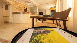 Zona de recepción de hotel con piso de mármol, mostrador de recepción y un área de descanso con una silla.