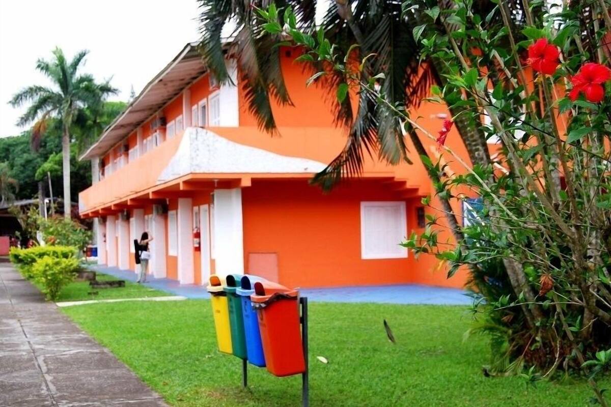 A building with a bright orange facade, a covered walkway, and a row of colorful trash bins.