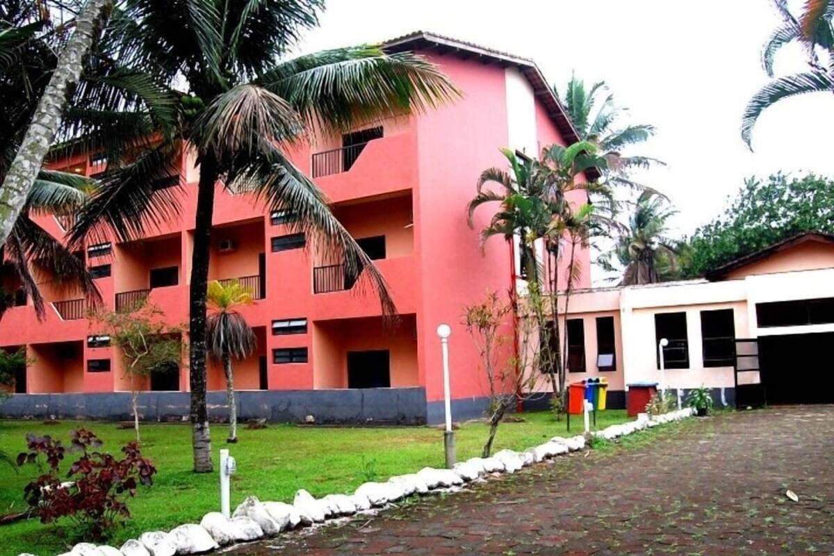 A multi-story building with a red facade, surrounded by palm trees and a paved walkway.