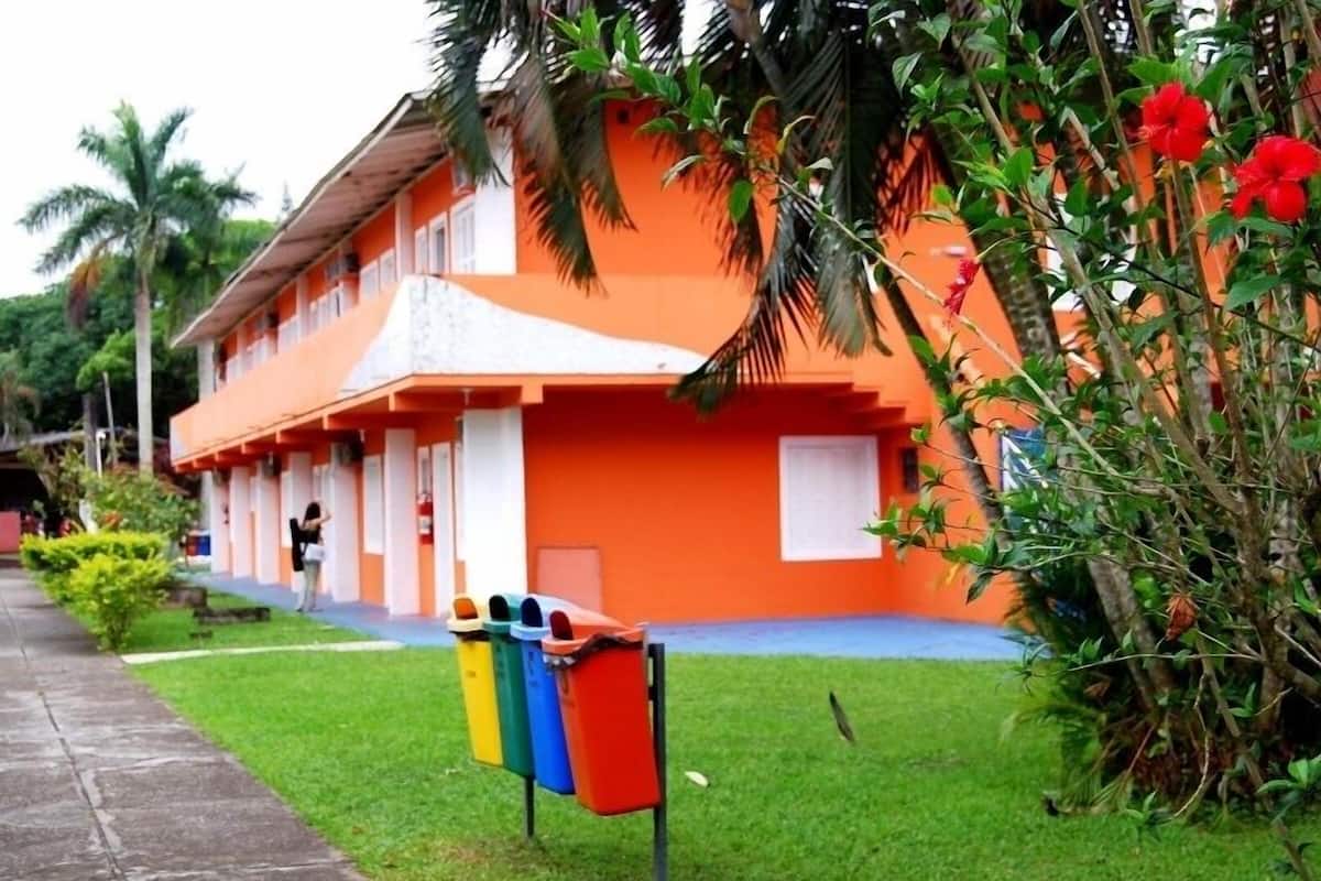 A two-story building with a bright orange facade, a covered walkway, and a row of colorful trash bins in front.