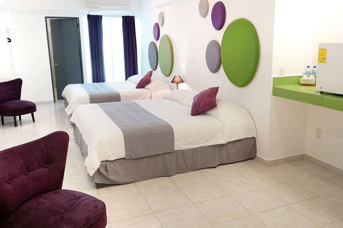 A hotel room with two beds, a purple armchair, a green counter, and a wall with circular decorations.
