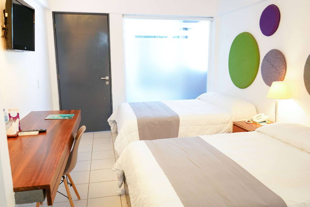 A hotel room with two beds, a desk, a chair, a TV, and a door.