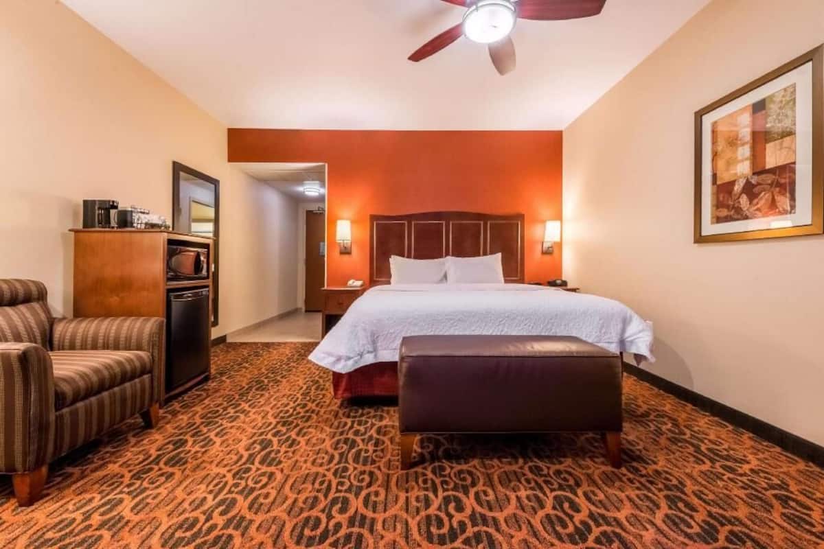 A hotel room with a bed, a chair, a desk, and a ceiling fan.