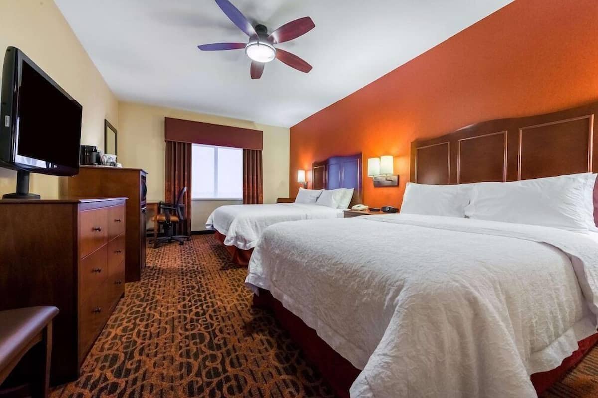 A hotel room with two beds, a television, a desk, and a ceiling fan.