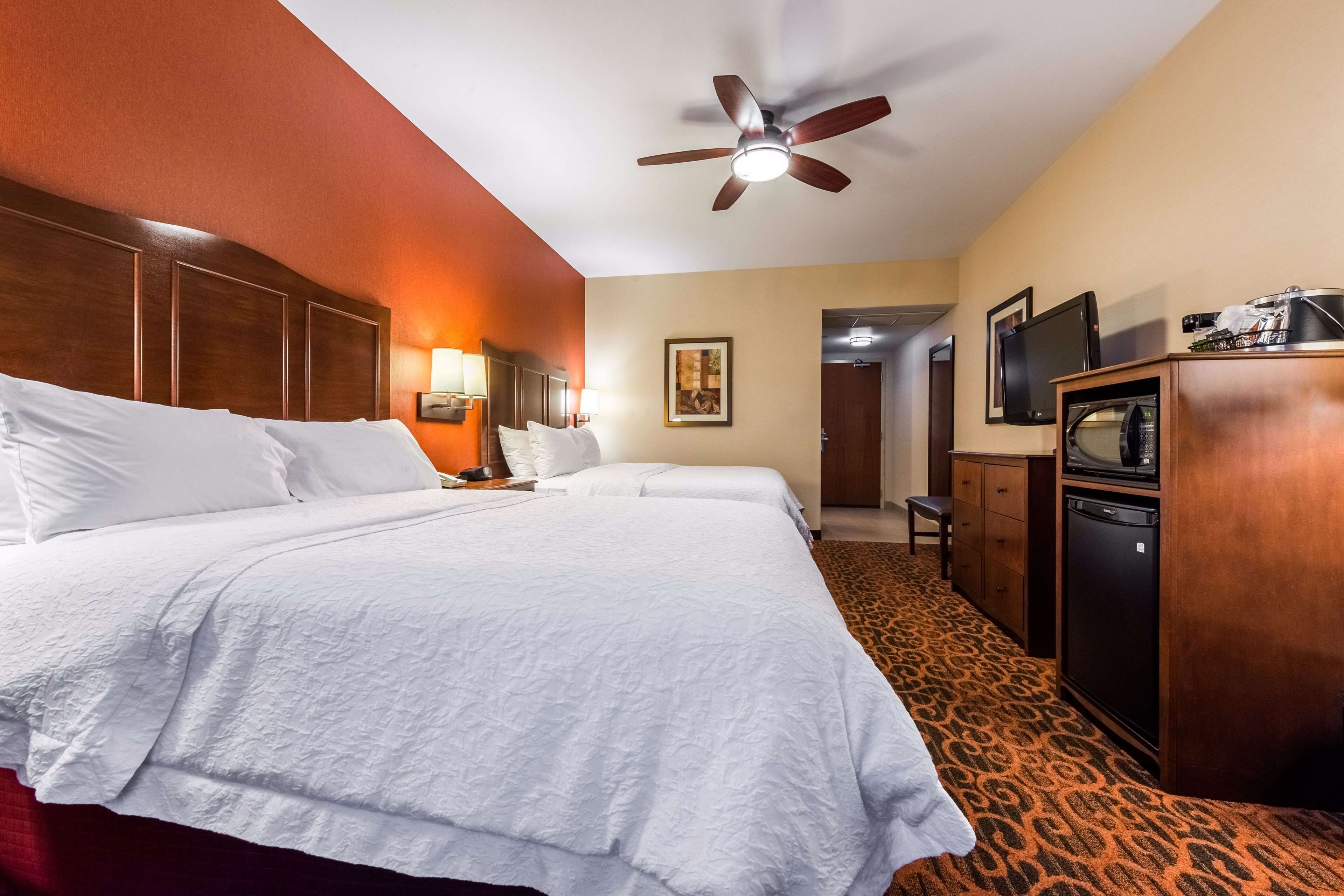 A hotel room with a large bed, a desk with a computer, a television, and a ceiling fan.