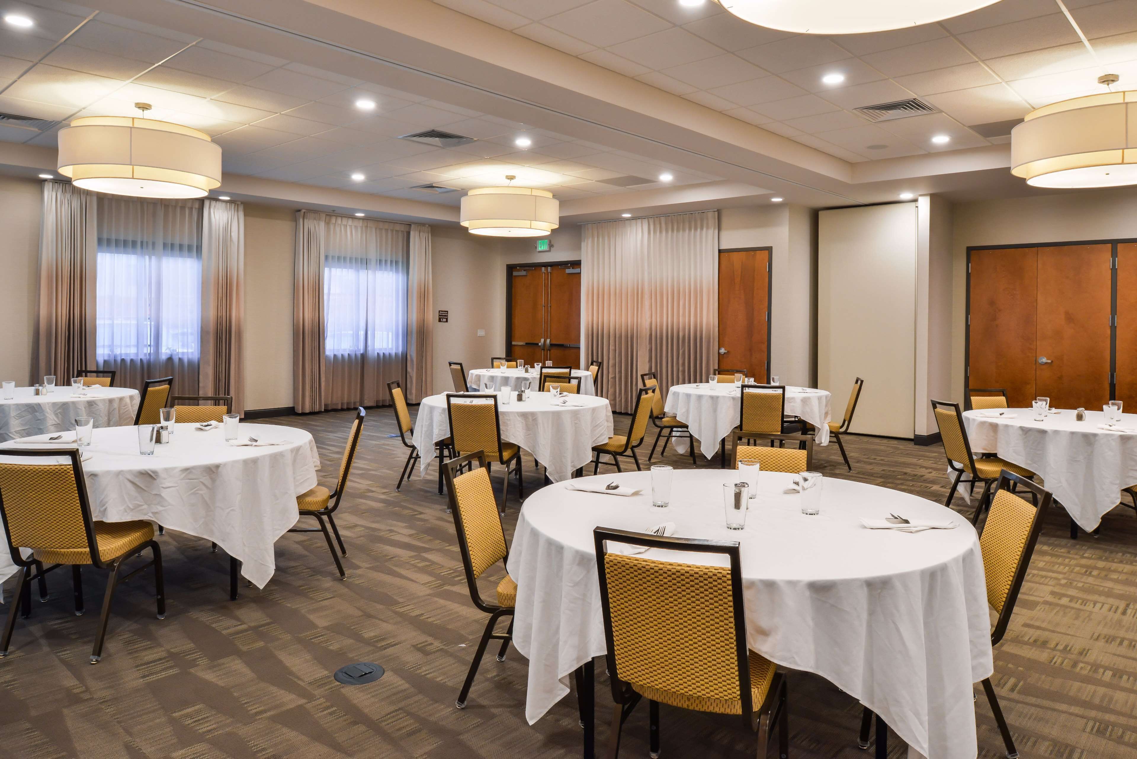A hotel conference room with multiple round tables, each covered with a white tablecloth, and equipped with chairs and dining essentials.
