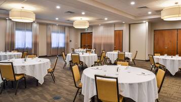 A hotel conference room with multiple round tables, each covered with a white tablecloth, and equipped with chairs and dining essentials.
