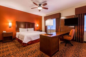 A hotel room with a bed, desk, chair, TV, and a ceiling fan.