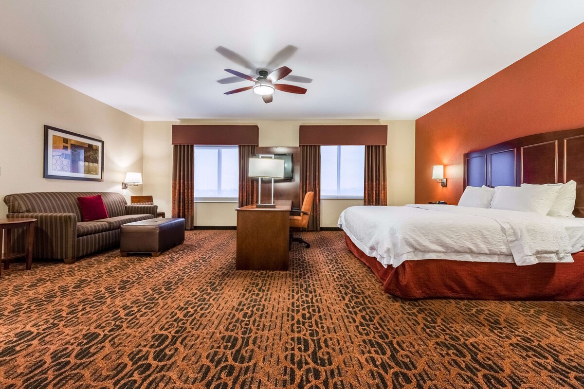 Una habitación de hotel con cama, sofá, escritorio, televisión y ventilador de techo.