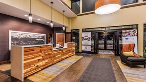 A reception desk with a wooden finish and a framed picture above it. There is a black leather chair with a yellow cushion to the right. - Hampton Inn & Suites Boulder-North (Boulder)