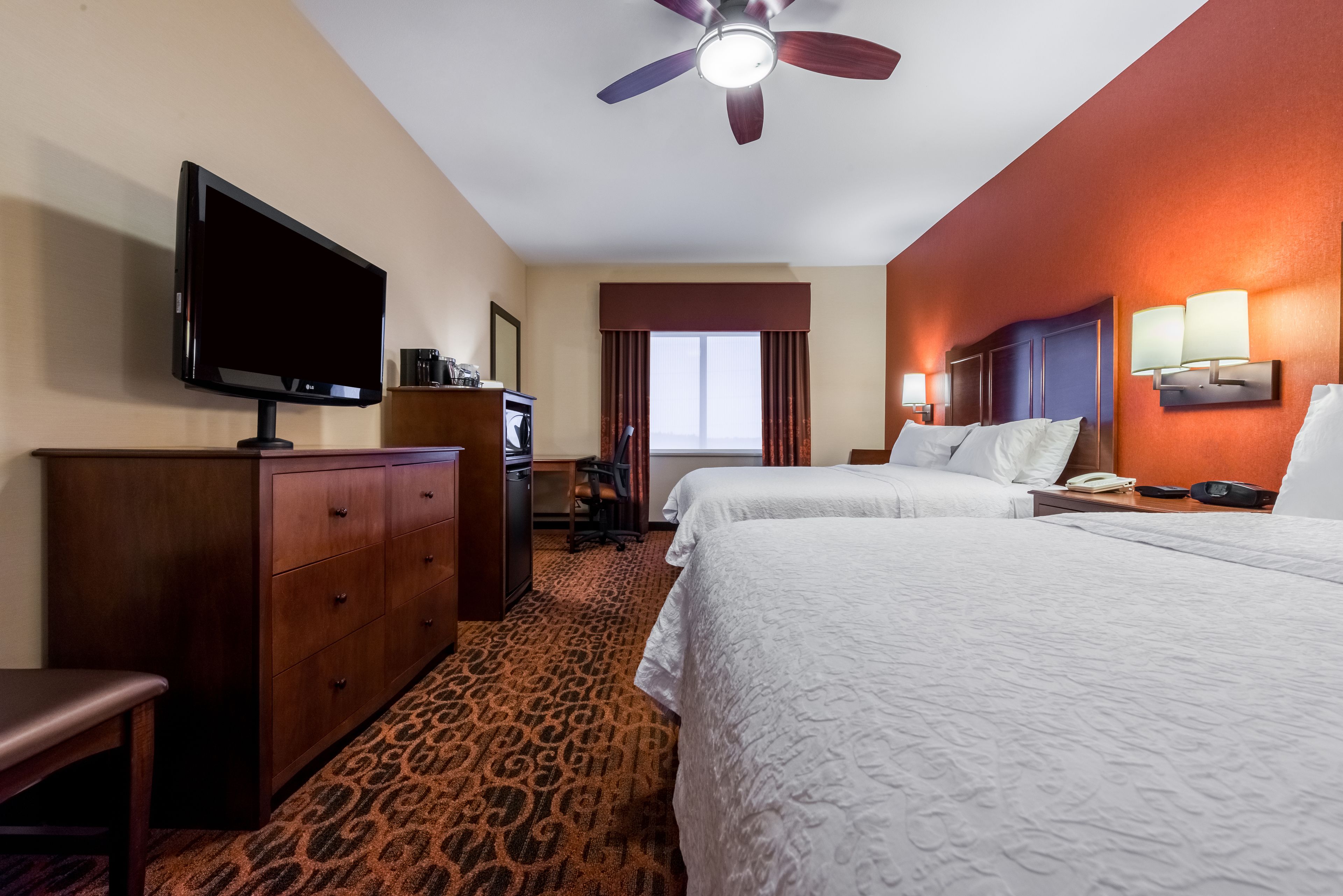 Quarto de hotel com duas camas, televisão, escrivaninha e ventoinha no teto.