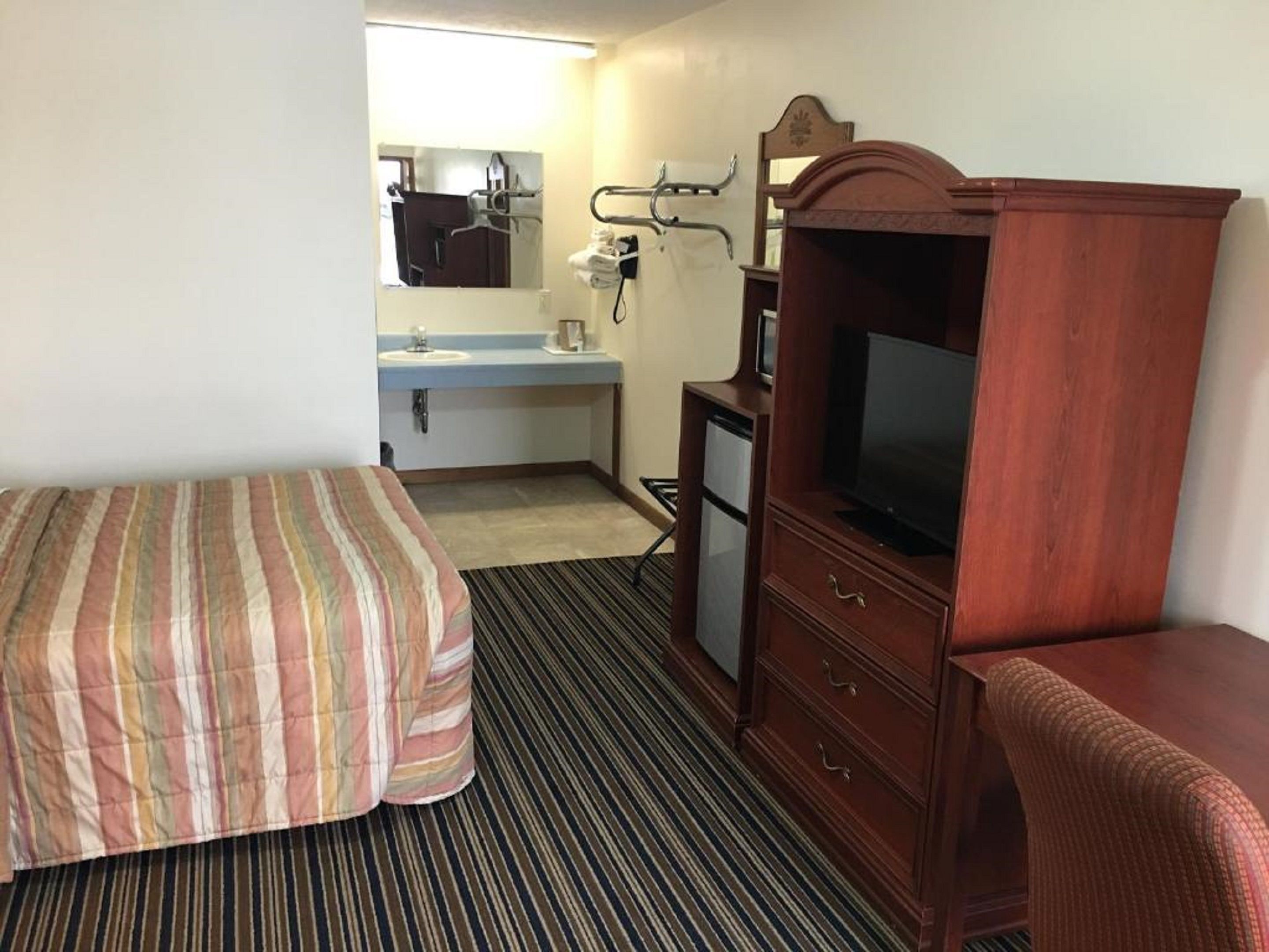 A hotel room with a bed, a TV, a desk, and a bathroom with a mirror and sink.