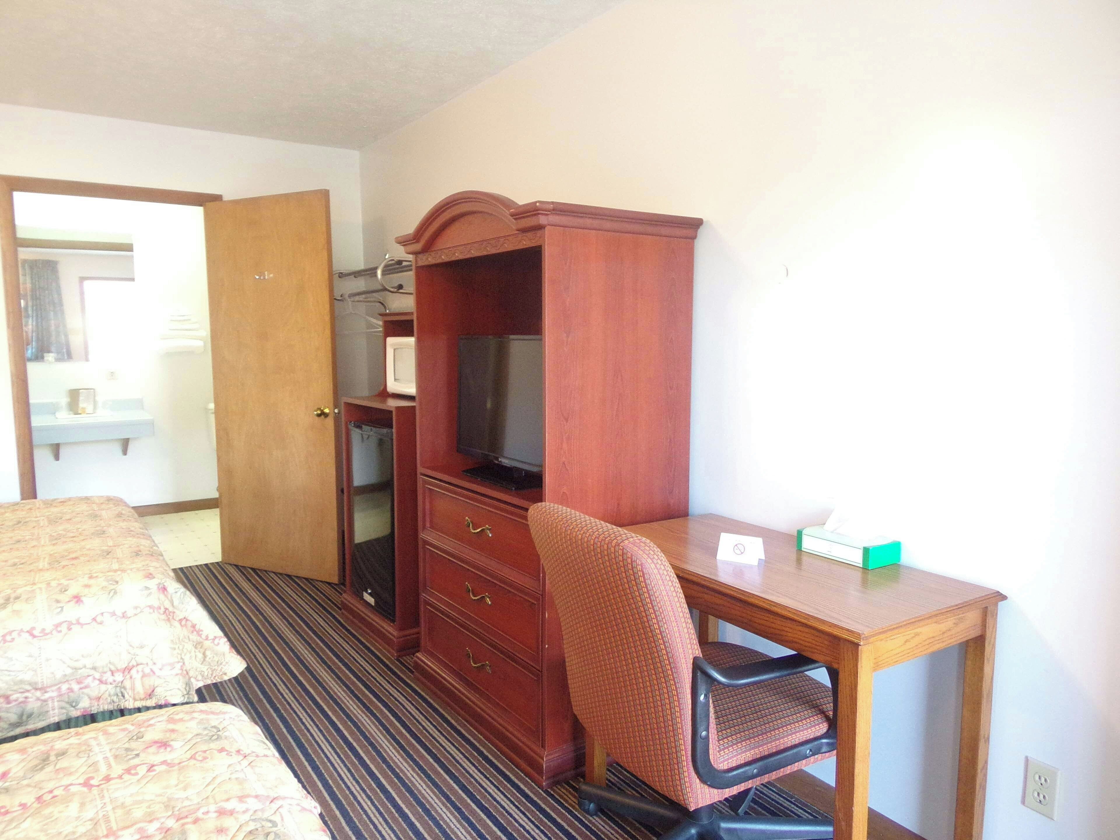 Quarto de hotel com cama, escrivaninha, cadeira, televisão e armário.