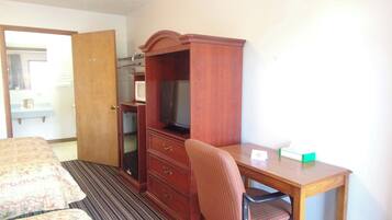 Quarto de hotel com cama, escrivaninha, cadeira, televisão e armário.
