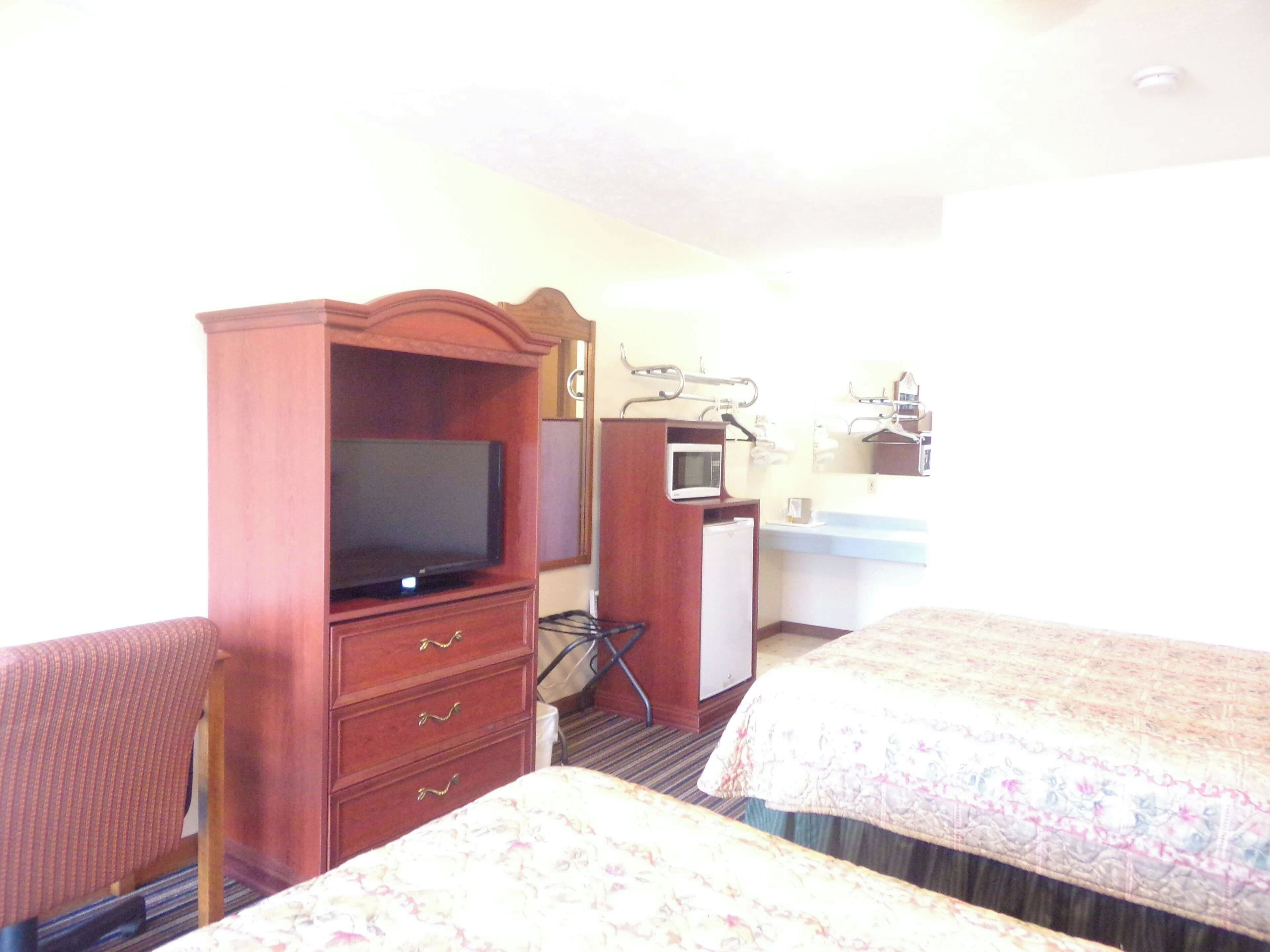 Een hotelkamer met een televisie, een magnetron, een klein bureau en twee bedden.