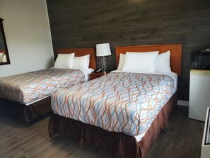 A hotel room with two beds, each with a patterned bedspread, wooden headboards, and a nightstand with a lamp. - Silverstar Motel (Midland)