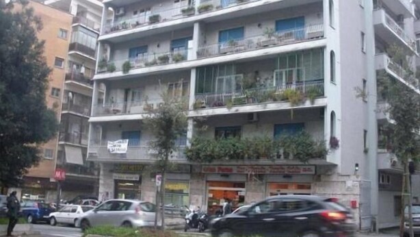 A multi-story building with balconies, storefronts, and parked cars. - Domina Romae B&B (Rome)