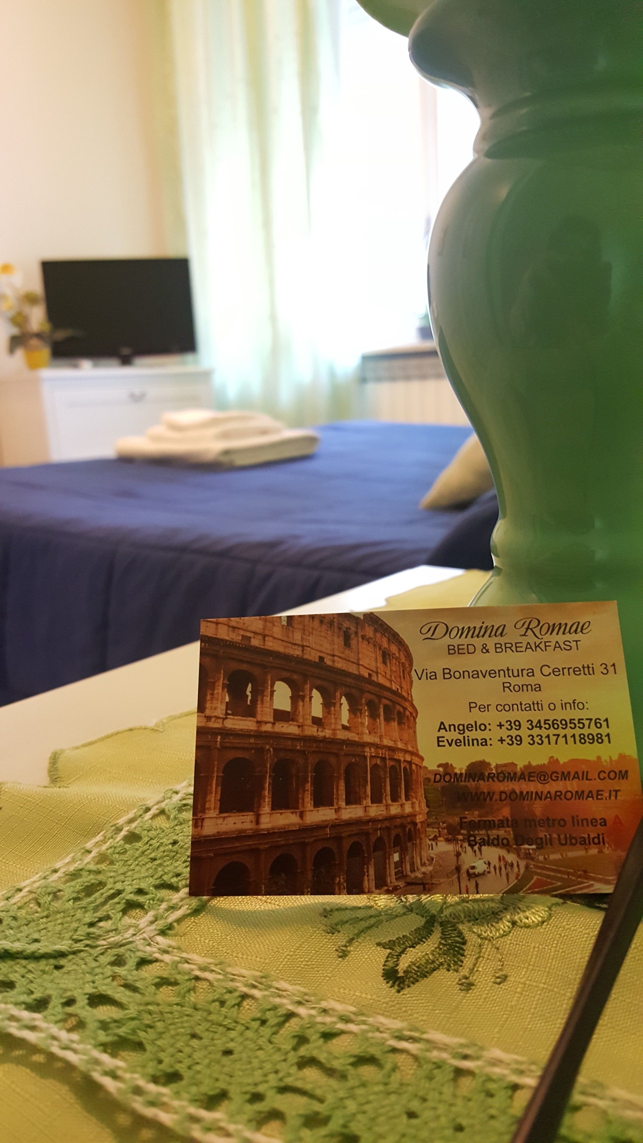 A room with a bed, a green vase, and a brochure featuring the Colosseum.