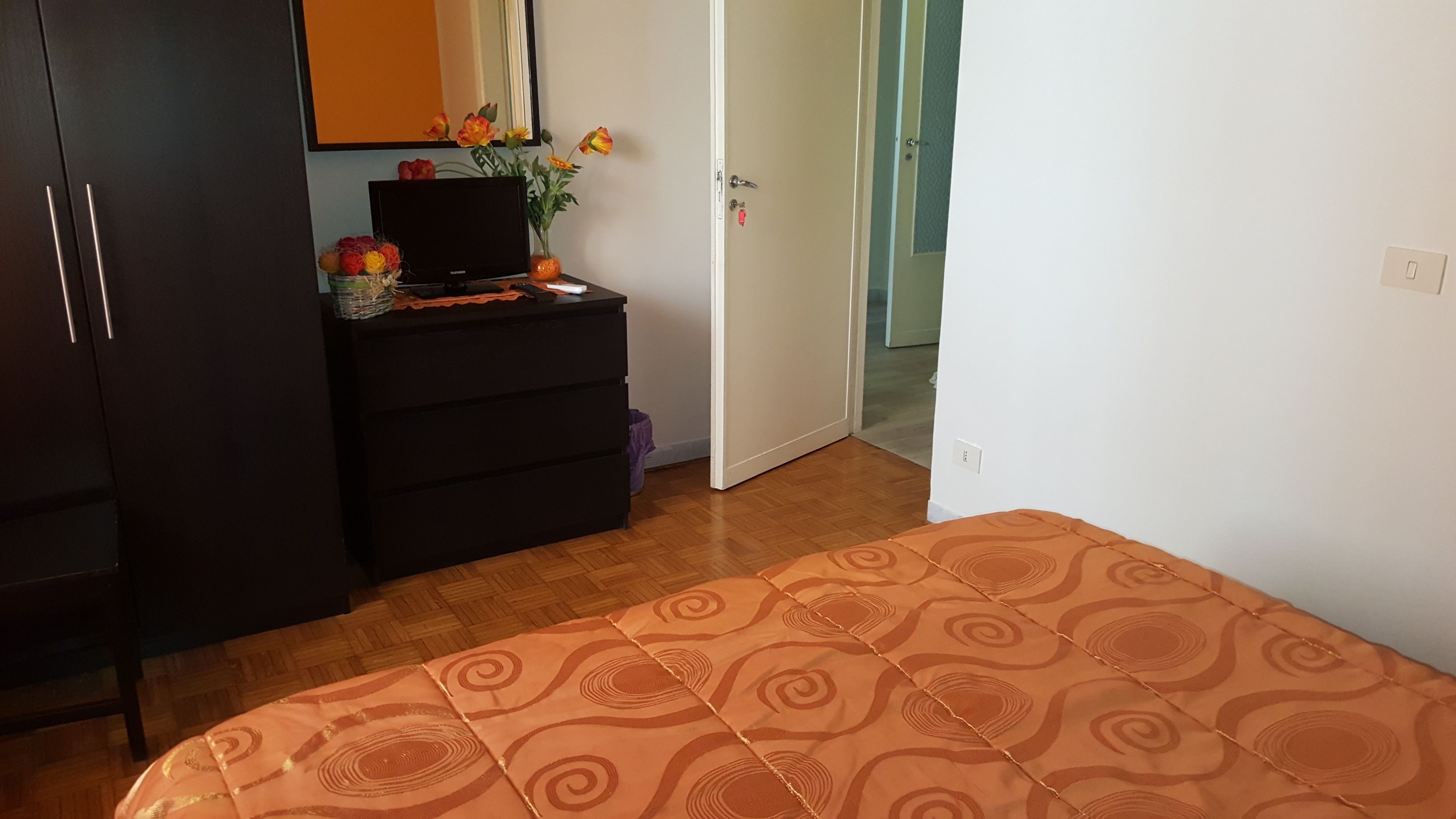 A bedroom with a bed, a dresser, a mirror, and a door leading to another room.