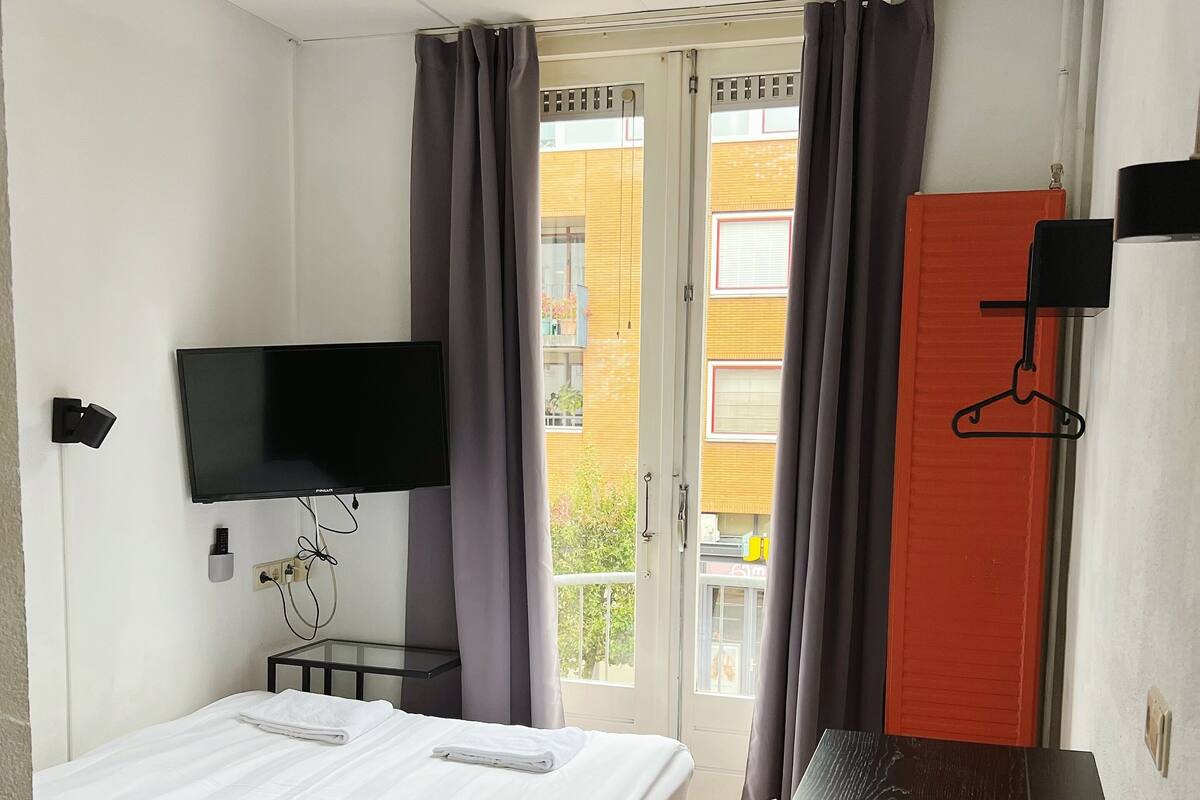 Une chambre d’hôtel équipée d’un lit, d’un bureau, d’une chaise, d’une télévision et d’une fenêtre avec des rideaux.
