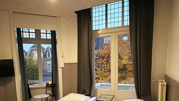 Et hotelværelse med to senge, et lille bord og udsigt udad.