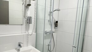 Et moderne badeværelse med en glasafskærmet brusekabine, en hvid vask og et spejl over vasken.
