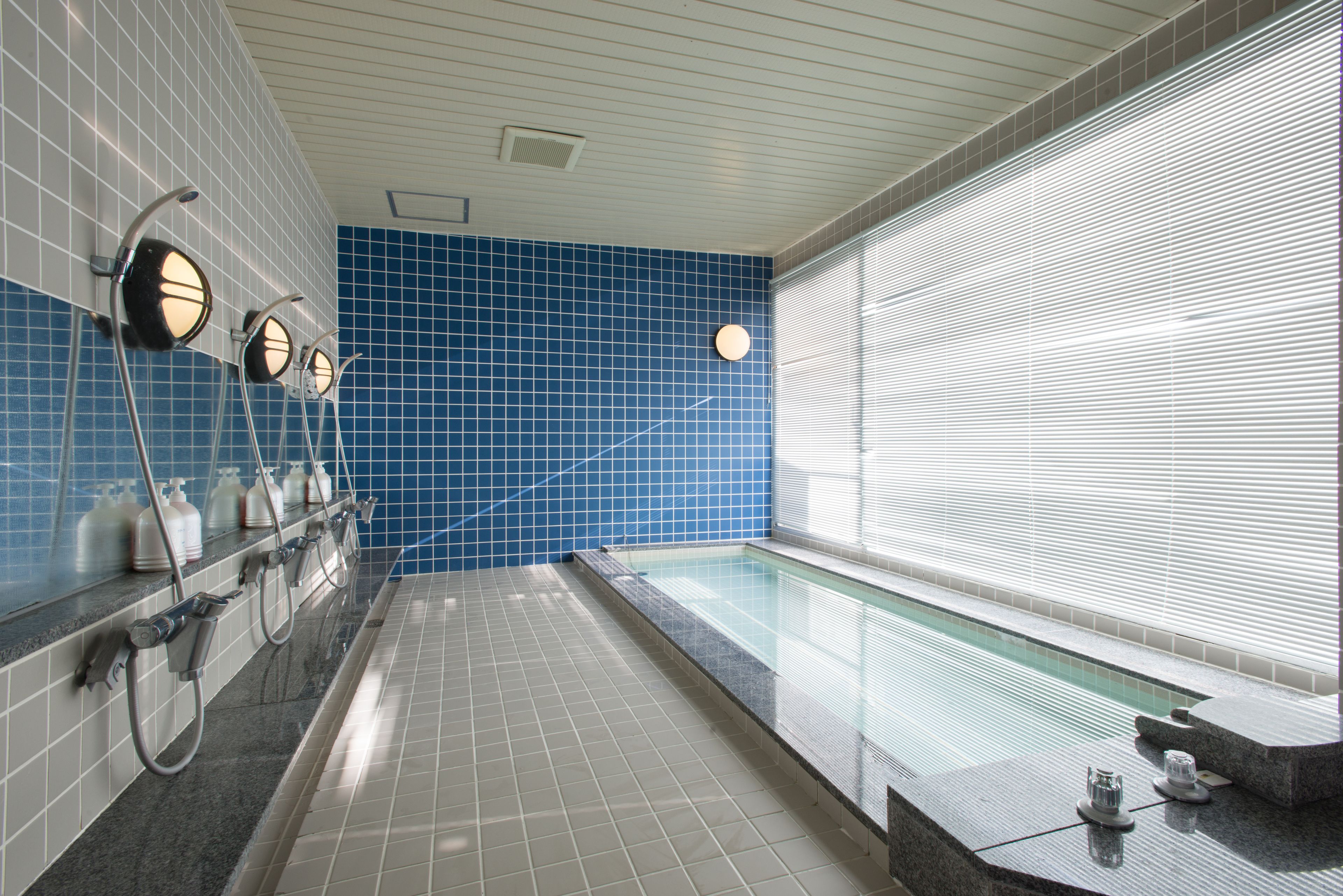 A swimming pool with a blue tiled wall, a long bench, and a row of hand dryers.