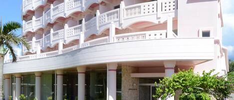 A multi-story hotel with balconies, a stone facade, and a paved entrance area.