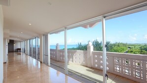 Un largo pasillo con amplias ventanas y un balcón con barandilla blanca.