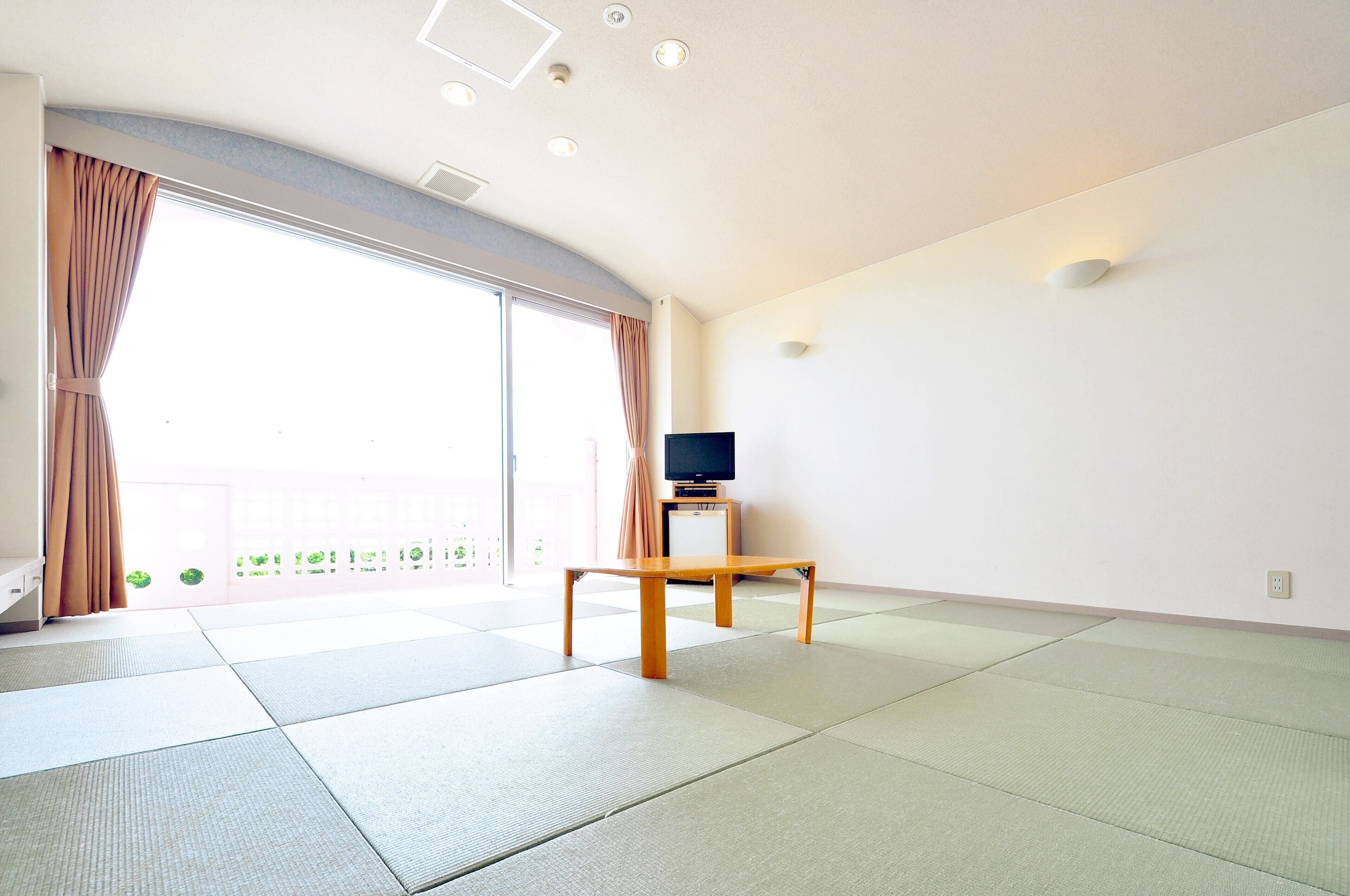 Una habitación con esteras de tatami, un televisor sobre un soporte y un ventanal corredero a un balcón.