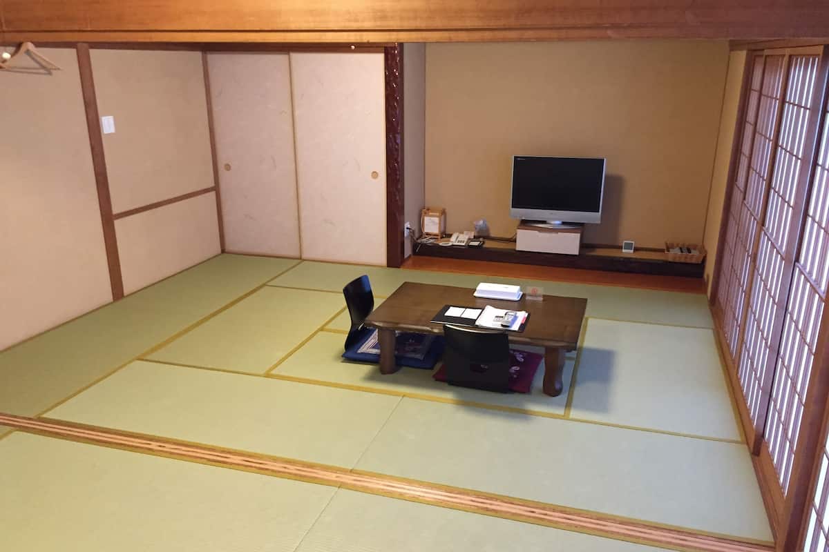 Een kamer met tatami matten, een lage tafel, een televisie en een klein bureau met stoel.