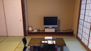Ein traditioneller japanischer Raum mit Tatami-Bodenbelag, einem niedrigen Tisch mit Fernseher und einer Schiebetür.