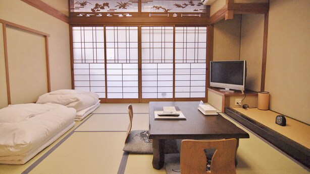 Ein traditioneller japanischer Raum mit Tatami-Boden, Futon-Bett, Schreibtisch mit Computer und Fernseher.