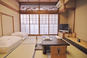 Ein traditioneller japanischer Raum mit Tatami-Boden, Futon-Bett, Schreibtisch mit Computer und Fernseher.