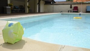 A swimming pool with a green bag on the edge, lounge chairs, and an umbrella in the background.
