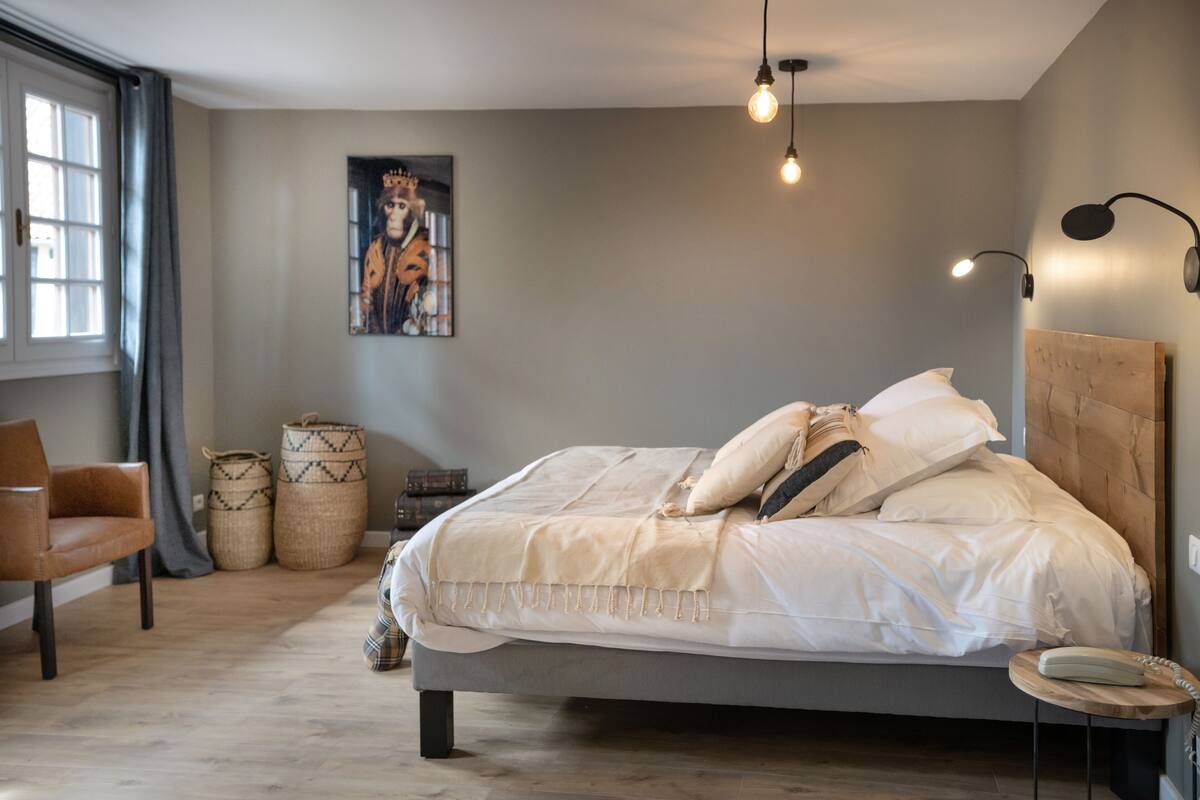 A modern bedroom with a large bed, a chair, a bedside table, and a wall-mounted lamp.