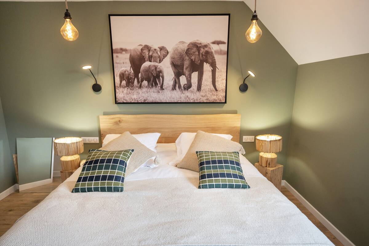 A bedroom with a large bed, two bedside lamps, a framed picture on the wall, and a wooden headboard.