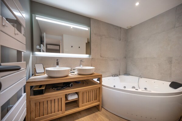 A modern bathroom with two sinks, a large bathtub, and a wooden vanity.