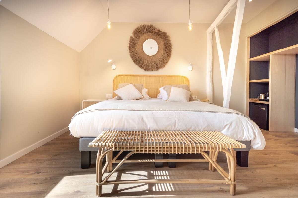A bedroom with a large bed, bedside tables, a bedside lamp, a wall-mounted mirror, and a wooden bench.
