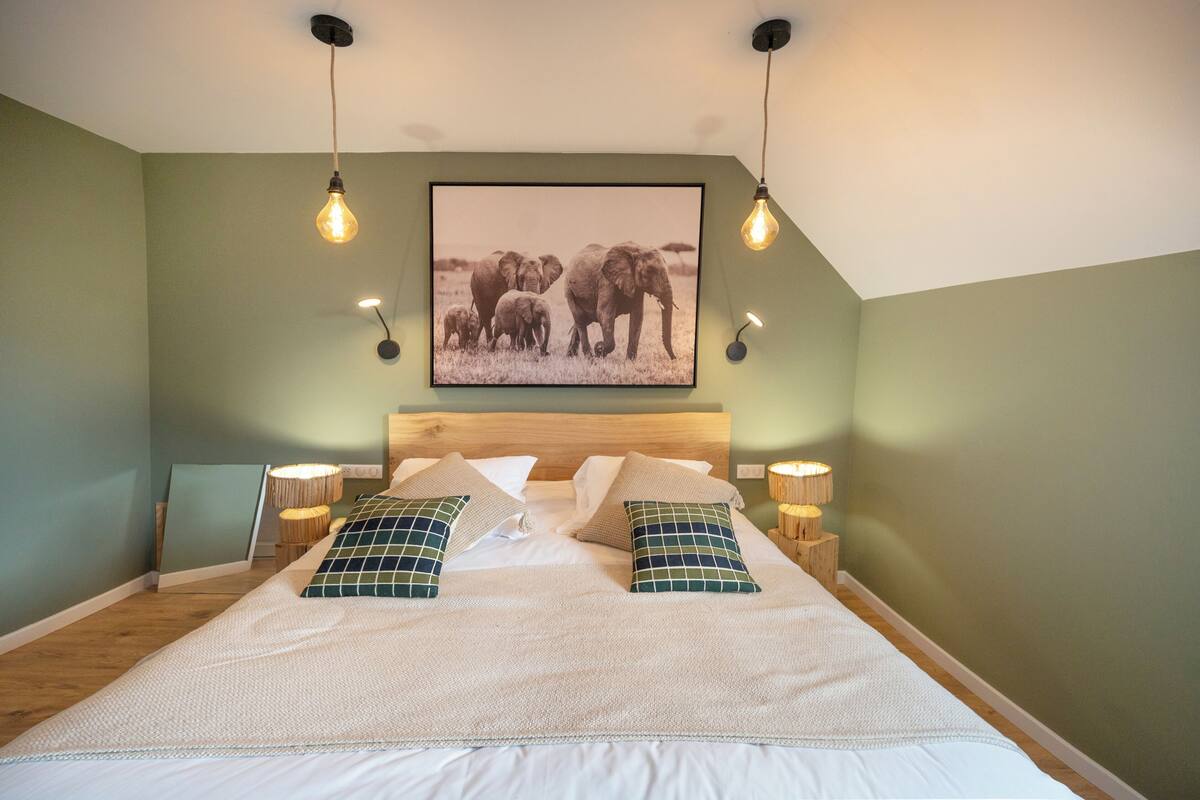 A bedroom with a large bed, two bedside lamps, a framed picture on the wall, and a wooden headboard.