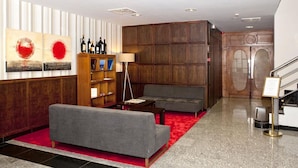 Eine moderne Lobby mit einer grauen Couch, Holzvertäfelung, einem Bücherregal und einem roten Teppich.