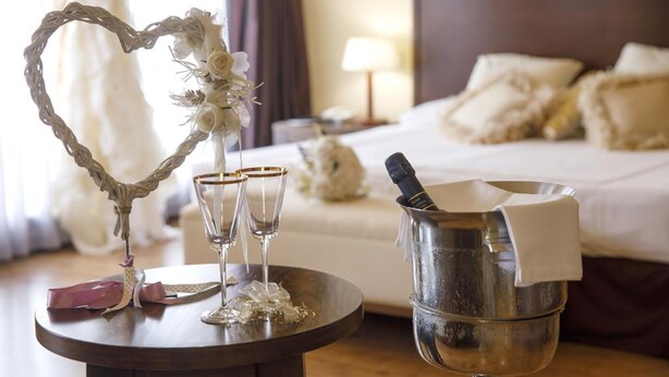 Ein Hotelzimmer mit einem Bett, einem Nachttisch mit Herz-Dekoration, zwei Gläsern und einem Eimer mit einer Flasche.