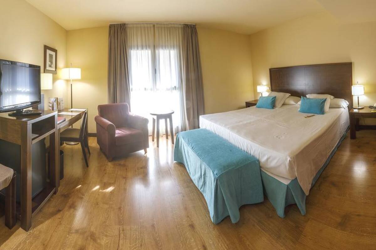 Ein Hotelzimmer mit einem Bett, einem Schreibtisch mit Fernseher, einem Sessel und einem kleinen Tisch.