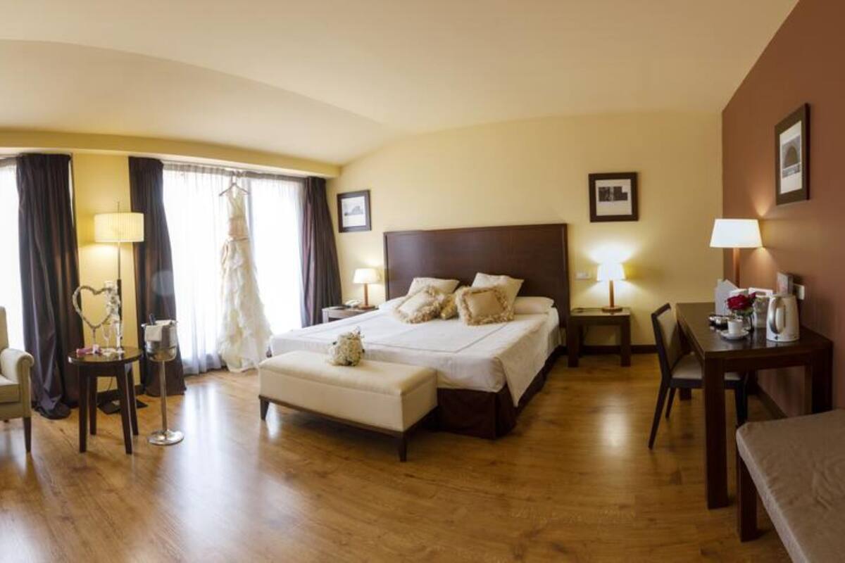 Ein Hotelzimmer mit einem großen Bett, einer Sitzecke mit Sofa und Sesseln, einem kleinen Tisch und einem Fenster mit Vorhängen.