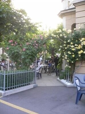 An outdoor cafe area with tables and chairs, surrounded by greenery and flowering plants. - Hotel Central Da Mario (Sursee)