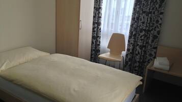 Una habitación sencilla y limpia con una cama, una silla y una pequeña mesa con una toalla.