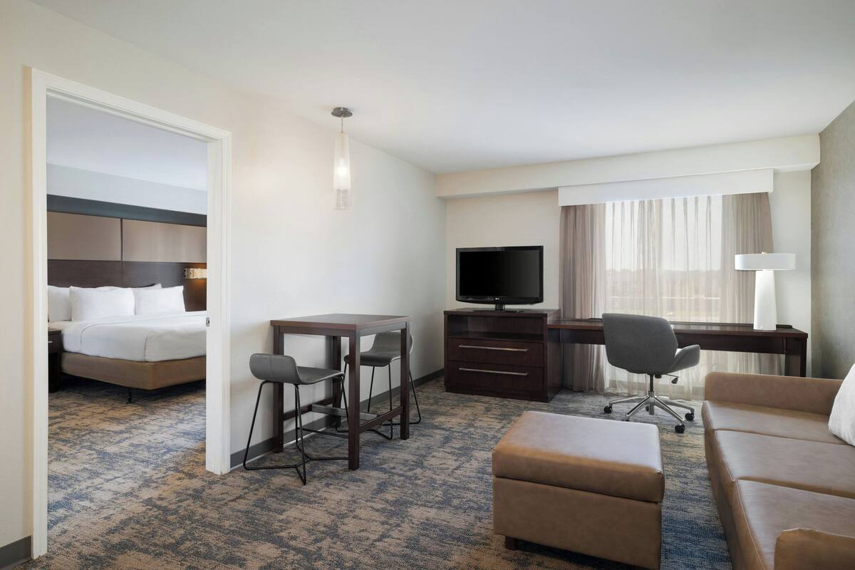A hotel room with a bed, a desk with a chair, a television, a sofa, and a small table.