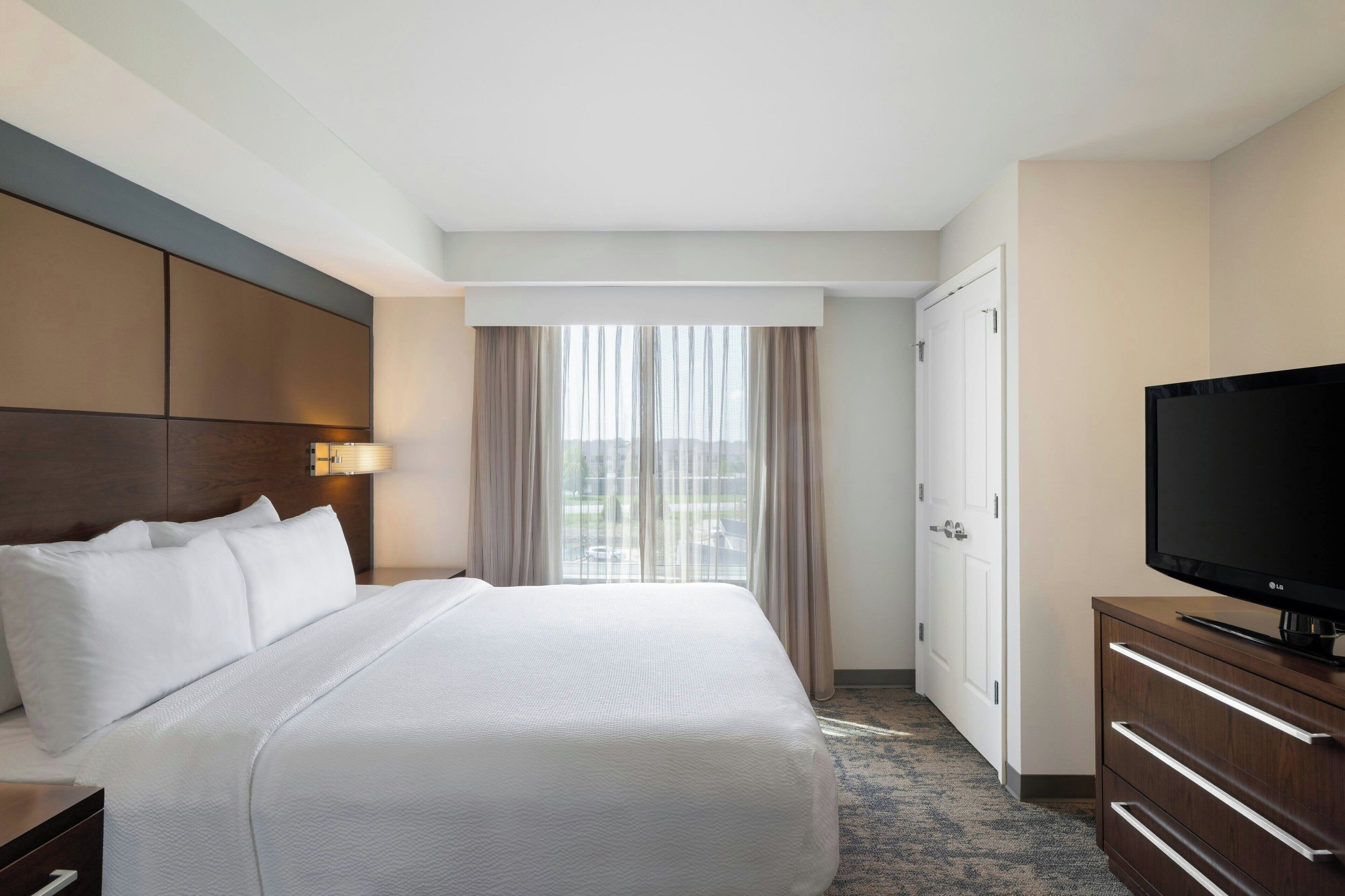 Habitación de hotel con una cama grande, televisión de pantalla plana, cómoda y ventana con cortinas.