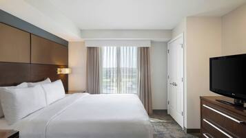Habitación de hotel con una cama grande, televisión de pantalla plana, cómoda y ventana con cortinas.